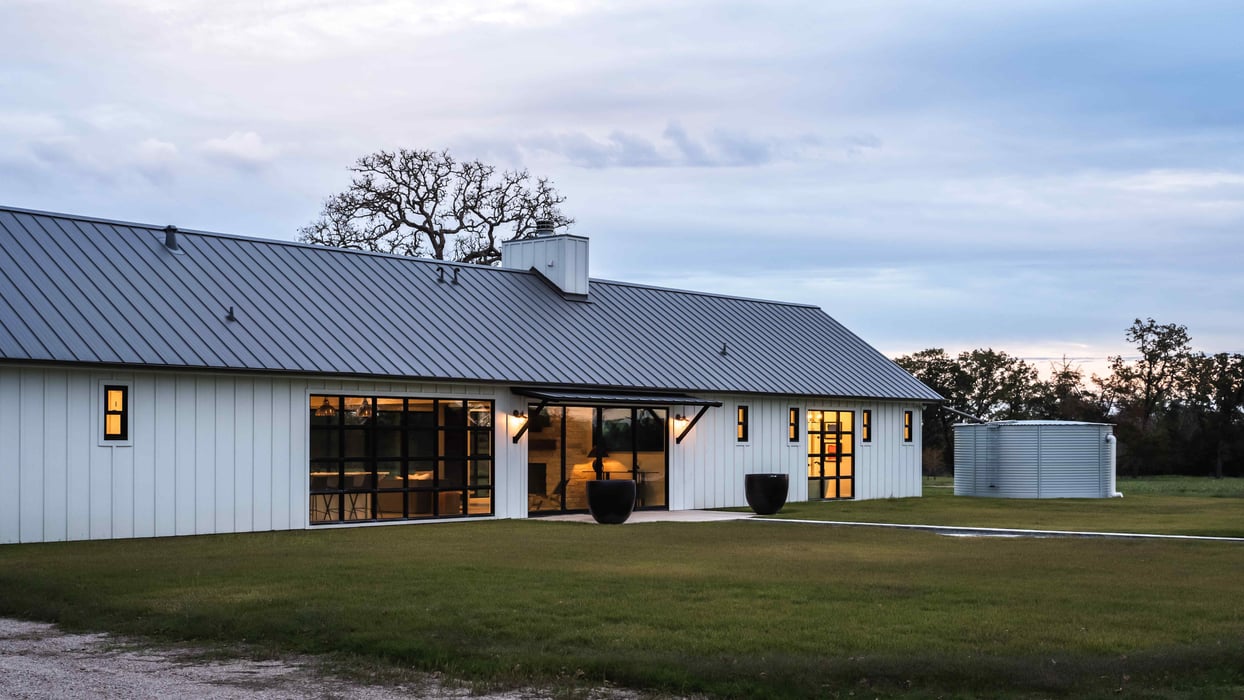 Side view of a modern farmhouse with a metal roof and outdoor planters. | J Bryant Boyd